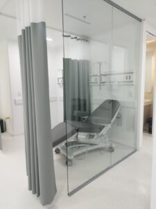 Sala de hospital con camilla y cortinas grises.